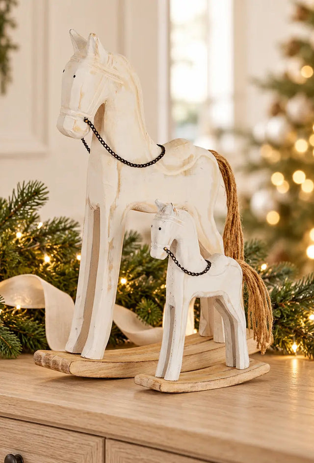 Two white wooden rocking horse decorations with brown manes, styled among lit Christmas greenery