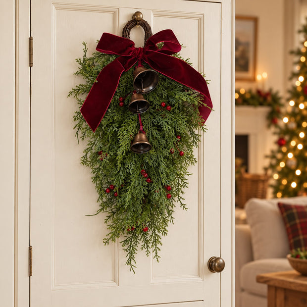 Spruce-style Christmas hanging swag with burgundy bow, red berries and bells on a cream door