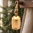 Large Brass Gold Cow Bell On Rope, gold-coloured bell hanging by rope from a wooden peg