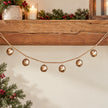 Gold sleigh bell garland draped beneath a wooden mantel with festive greenery.