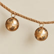 Two gold sleigh bells with snowflake cut-outs hanging from natural twisted cord.