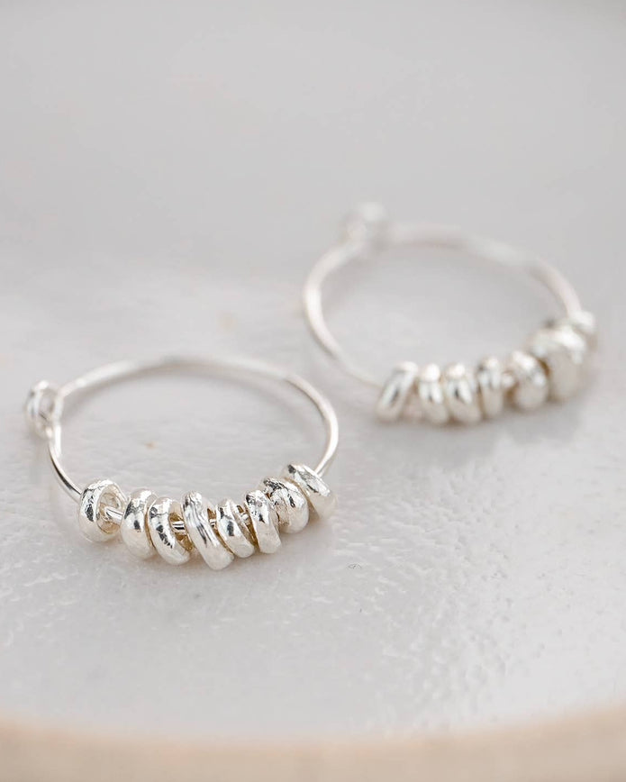 Silver hoop earrings with bead detailing on a light background
