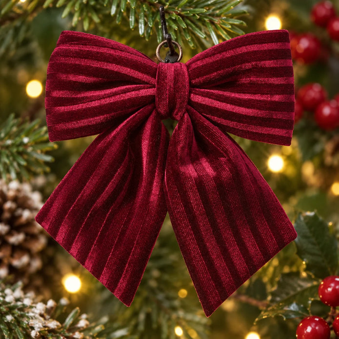 Small burgundy velvet bow with textured stripes against festive greenery.