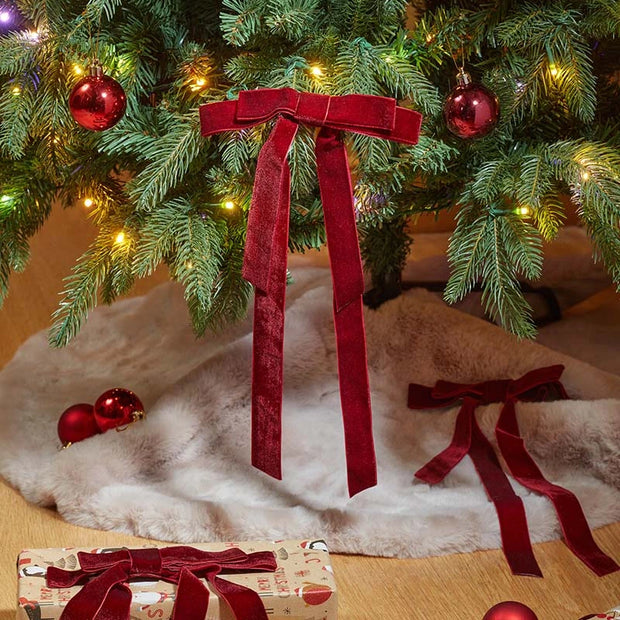 Burgundy long-tail velvet bows decorating Christmas tree branches, with further bows below.