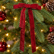 Burgundy long-tail velvet bow among green branches and warm Christmas lights.