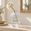 Glass acorn vase with a white flower by a mirror