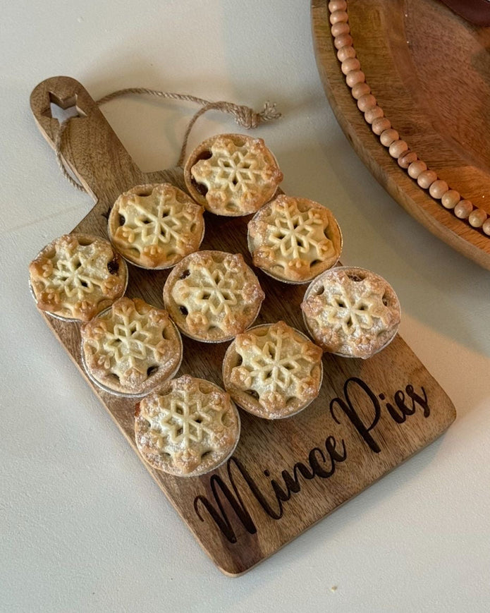 Wooden board with mini pies and 'Mince Pies' inscription on a white surface