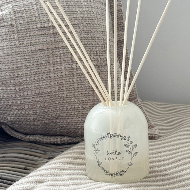 Beige Moments Clear Glass Reed Diffuser -  Hello Lovely, Hello Lovely reed diffuser on a striped throw