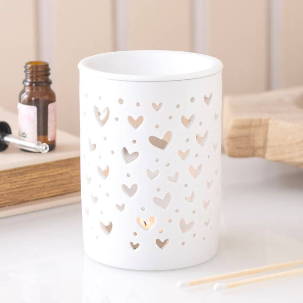 White Heart Cut Out Oil Burner and Wax Warmer, white cylindrical heart-cutout burner glowing on a table