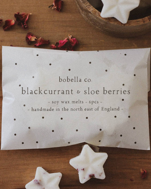 Star-shaped candles with a packaging label on a wooden surface with dried flowers.