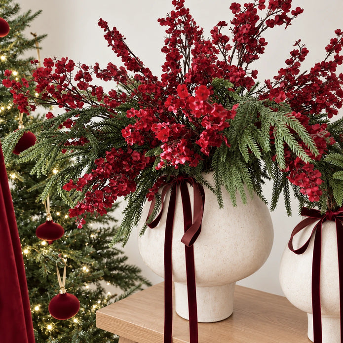 Burgundy gypsophila and greenery arranged in cream vases beside a Christmas tree.