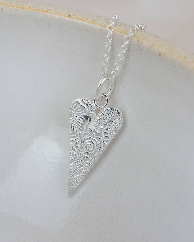 Silver heart-shaped pendant on a chain against a light background
