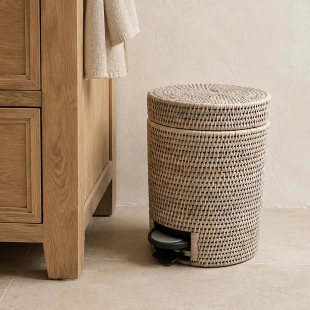 Wickham Rattan Round Pedal Waste Paper Bin, closed woven pedal bin beside a wooden cabinet