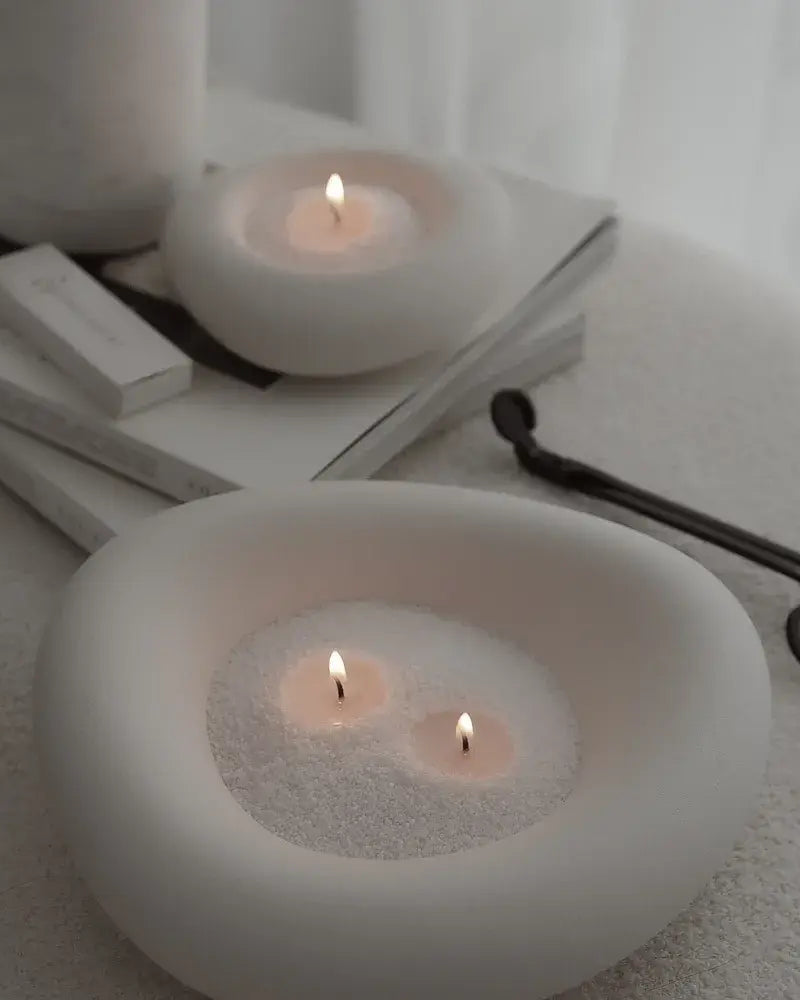 Two white ceramic candle holders with lit candles on a white surface.