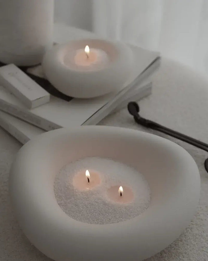 Two white ceramic candle holders with lit candles on a white surface.