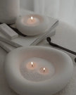 Two white ceramic candle holders with lit candles on a white surface.