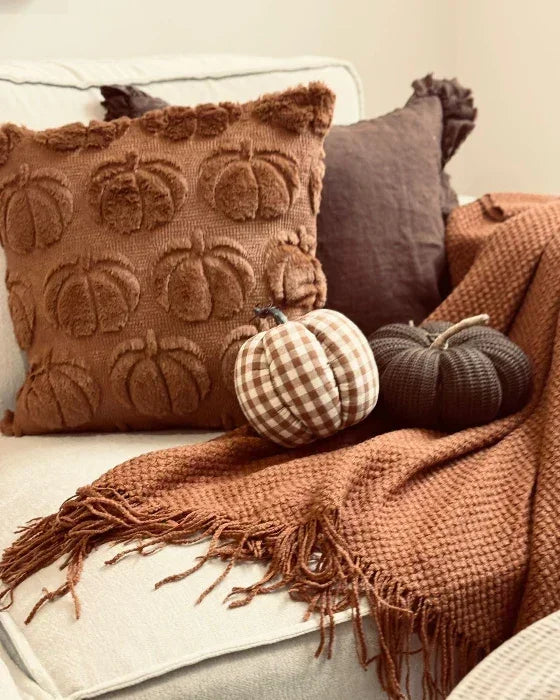 Decorative pillows with pumpkin pattern on a couch with a blanket and pumpkins.