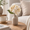 Artificial Short Soft Cream Hydrangea Stem, cream hydrangea in a taupe vase beside a mug and sofa