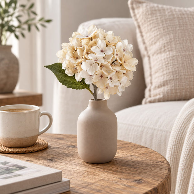 Artificial Short Soft Cream Hydrangea Stem, cream hydrangea in a taupe vase beside a mug and sofa