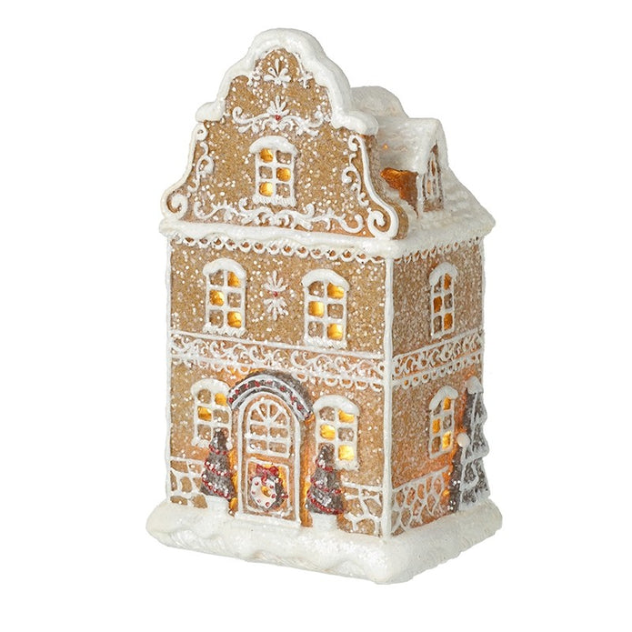Tall gingerbread house with miniature trees and glowing windows on a white background