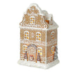 Tall gingerbread house with miniature trees and glowing windows on a white background