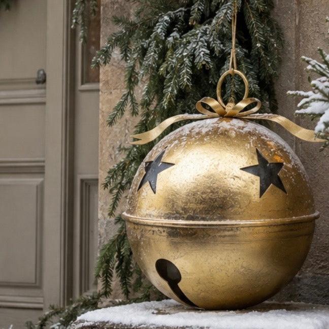 Gold Metal Hanging Bell With Cut Out Stars, close-up of a gold bell beneath snowy greenery
