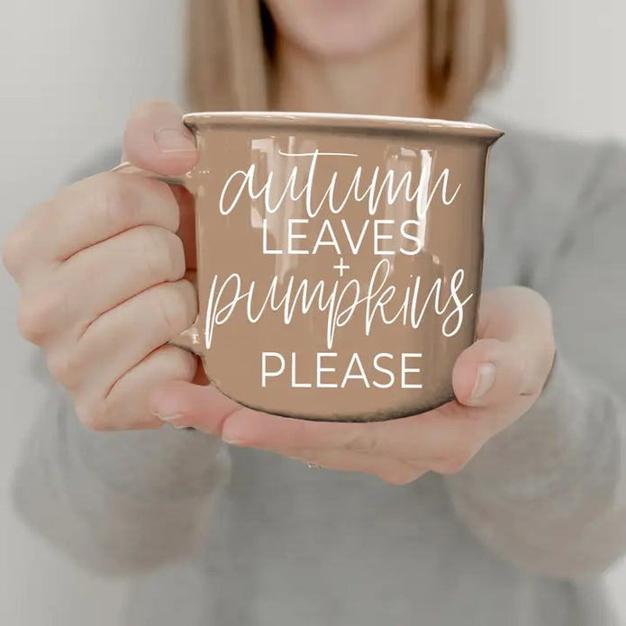 Person holding a mug with 'Autumn leaves + pumpkins please' text.
