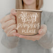 Person holding a mug with 'Autumn leaves + pumpkins please' text.