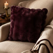 Burgundy Luxury Faux Fur Cushion, burgundy faux fur cushion on a cream armchair beside a candle