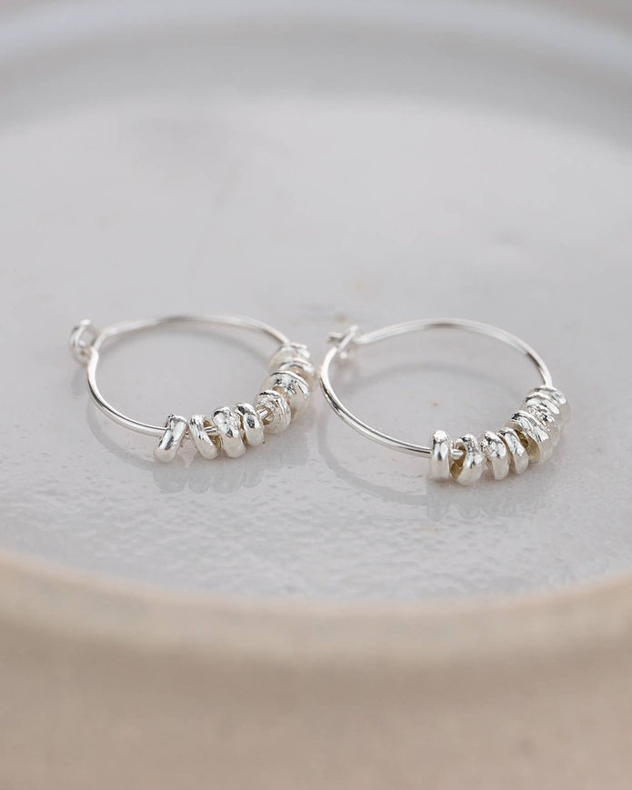 Silver hoop earrings with small pearls on a light gray plate