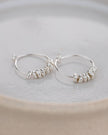 Silver hoop earrings with small pearls on a light gray plate
