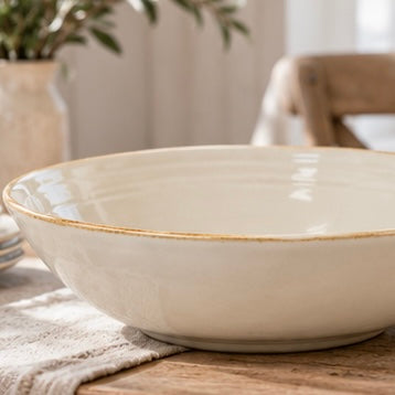 Close view of an empty ivory stoneware salad bowl with a brown-edged rim on a linen-covered table