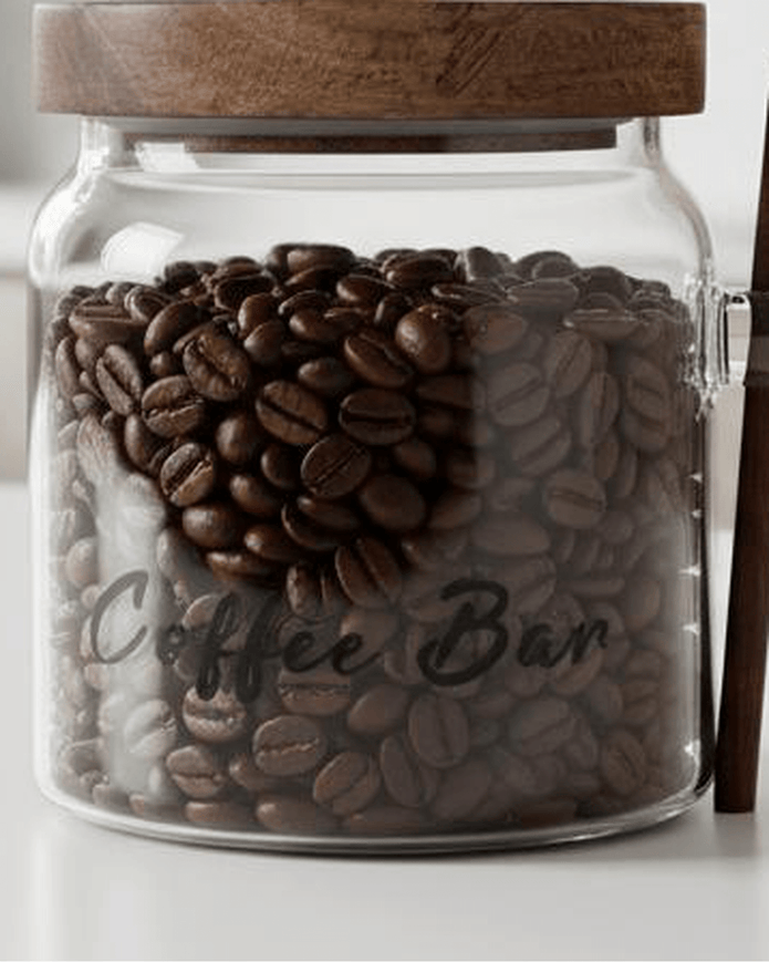 Clear glass coffee storage jar with dark wood lid and matching spoon, ideal for kitchen and dining organization.