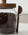 Glass coffee storage jar with dark wood lid and spoon, ideal for kitchen and dining, by Starlight Express.
