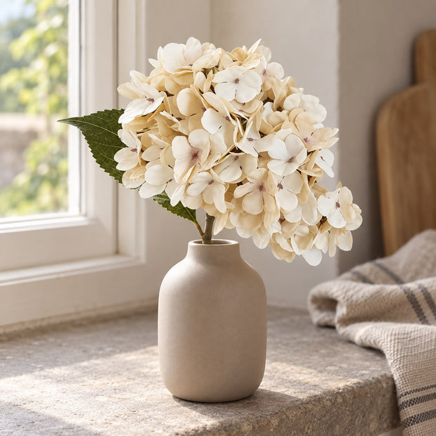 Artificial Short Soft Cream Hydrangea Stem, cream hydrangea stems in a taupe vase beside a window