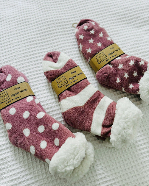 Three pairs of pink slipper socks with white polka dots and stripes on a textured surface.