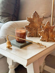 Candle Snuffer - Gold, gold-coloured candle snuffer beside a candle and leaf ornaments