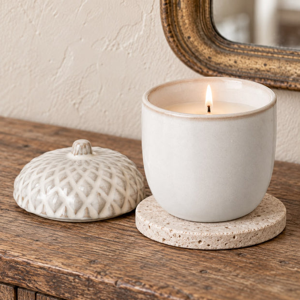 White Porcelain Acorn Candle Pot, lit white acorn candle pot and lid on a round coaster