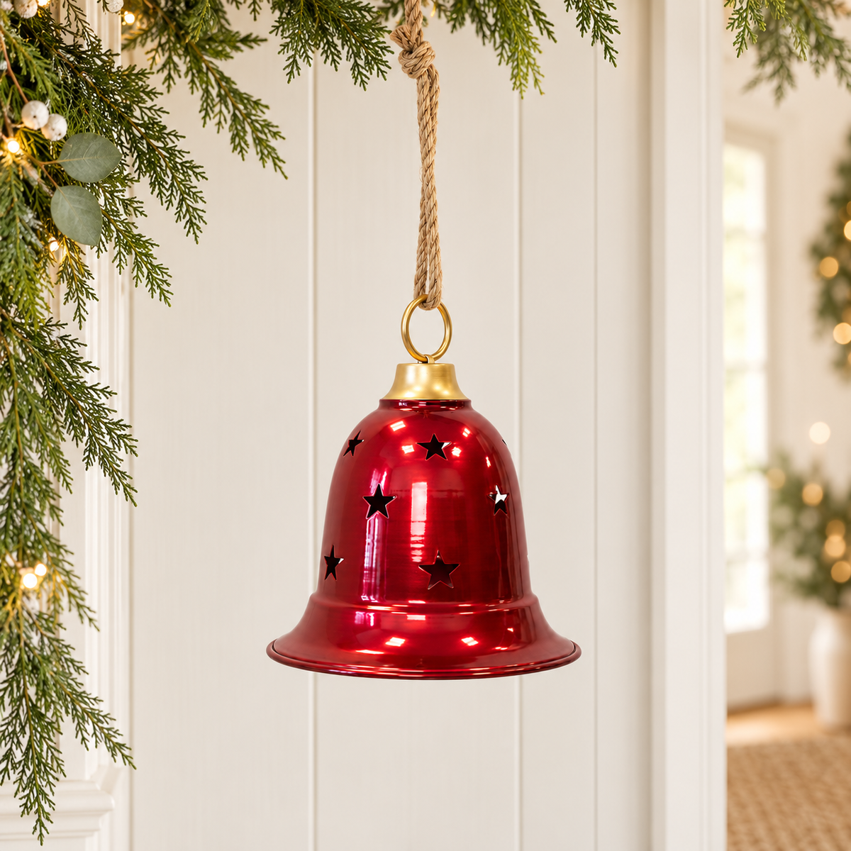 Glossy burgundy metal bell with star cut-outs hanging from rope beside Christmas greenery