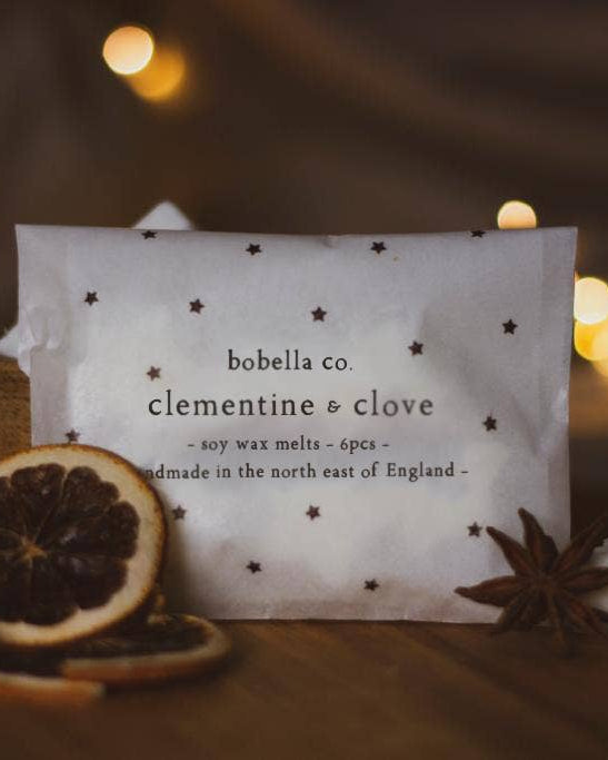 Candle labeled 'bobella co. clementine & clove' with decorative elements on a warm background.