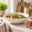 Ivory stoneware salad bowl with a brown-edged rim holding a mixed salad on a kitchen counter