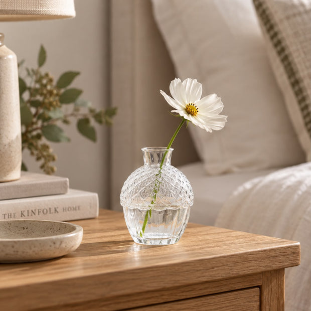 Glass acorn vase with a white flower by a bed