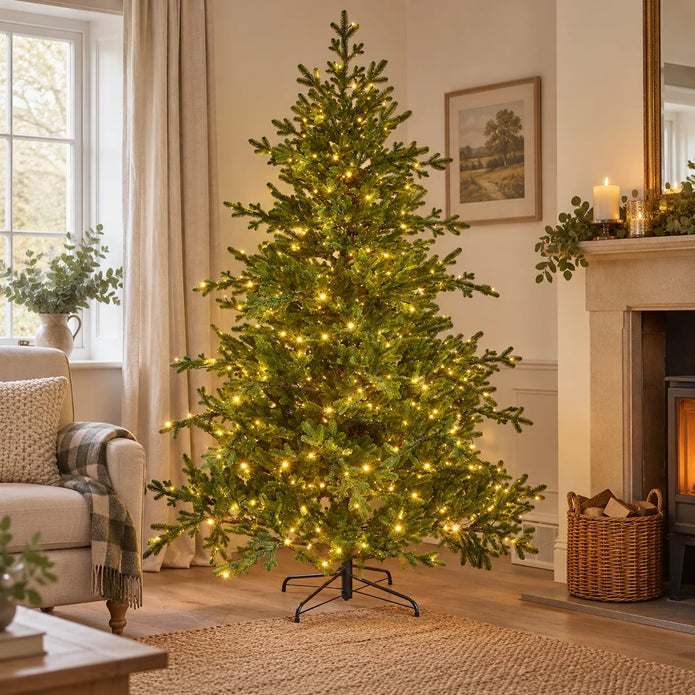 Illuminated green InLit Regal KingTree Christmas tree beside an armchair and fireplace.