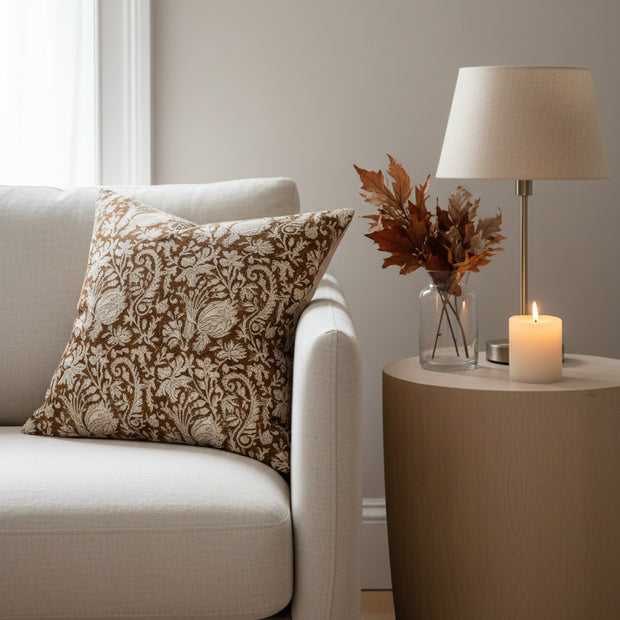 A square decorative throw pillow featuring an intricate floral damask pattern in brown and cream, set against a plain white background.