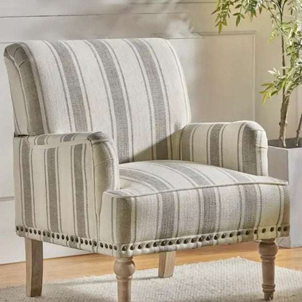 Neutral beige striped armchair with nailhead trim and turned wooden legs beside a plant.