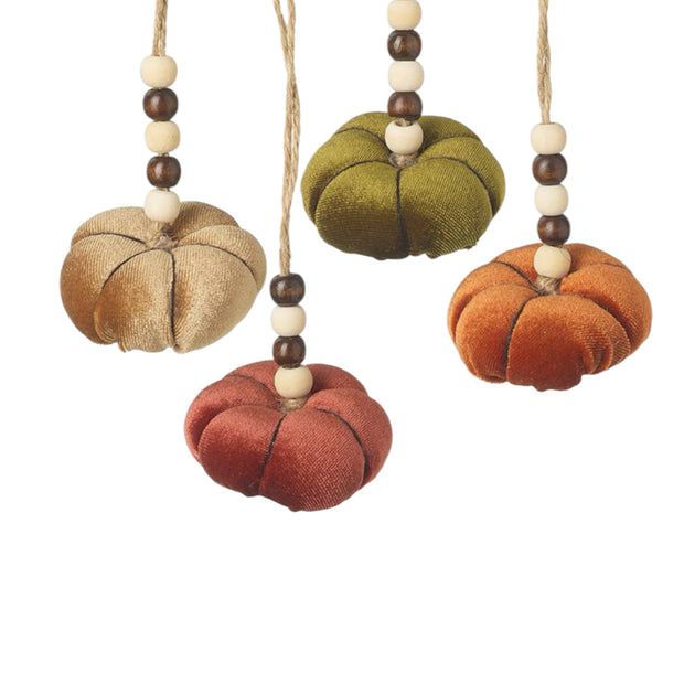 Four velvet pumpkin-shaped hanging ornaments in beige, olive green, rust red, and burnt orange, each suspended from a string with wooden beads, shown on a white background.