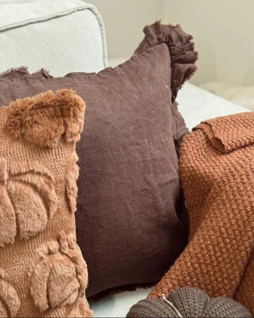 Cozy arrangement of textured pillows and a blanket on a sofa.