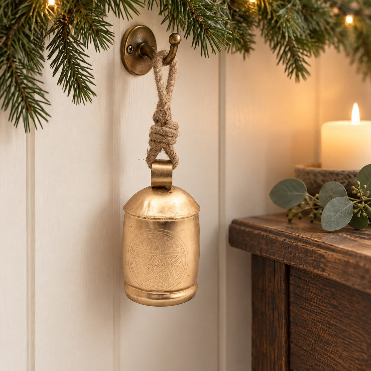 Large Brass Gold Cow Bell On Rope, gold-coloured bell hanging beside a candlelit console