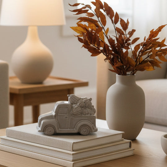 Two silver-toned vintage pickup truck figurines carrying bundles of Christmas trees, displayed on a light gray surface against a white paneled background.