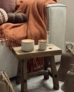 Cozy living room with a wooden stool, candles, and a blanket on a sofa.